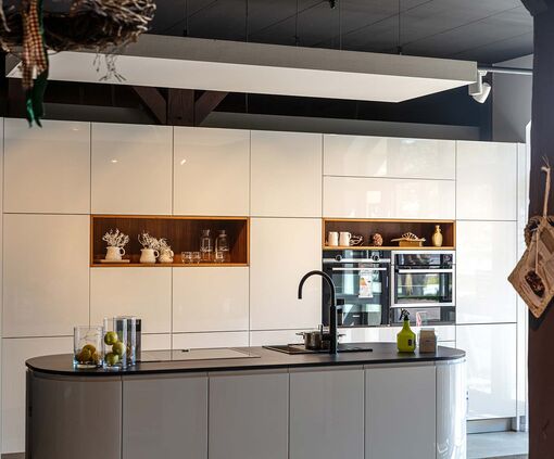 Moderne weiße Küche mit grifflosen Fronten, Holzeinsätzen und ovaler grauer Kücheninsel